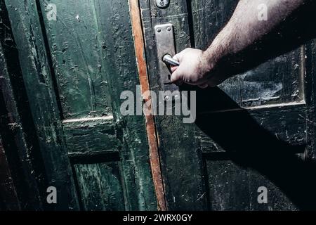 Photo d'un homme saisissant et ouvrant une vieille porte poussiéreuse obsolète. Concept d'horreur. Banque D'Images