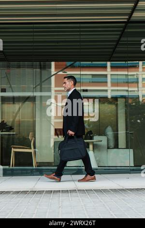 Portrait vertical pleine longueur d'un homme d'affaires mature marchant et tenant un sac d'ordinateur portable. Homme dirigeant financier adulte moyen qui va au bureau. Beau homme d'affaires d'entreprise avec une mallette. Photo de haute qualité Banque D'Images