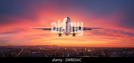 L'avion vole dans un ciel coloré au-dessus de la ville la nuit Banque D'Images