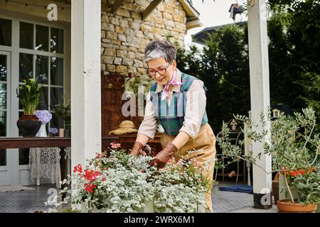Belle femme mature chic avec des lunettes prenant soin de ses fleurs près de sa maison en Angleterre Banque D'Images