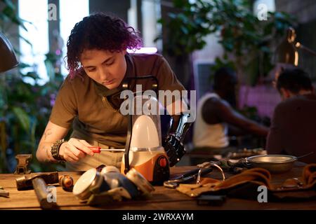 Plan de mise au point sélective d'une jeune femme caucasienne handicapée debout à table assemblant une lampe portable à l'aide d'un tournevis Banque D'Images