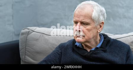 Homme âgé avec une expression triste assis seul sur le canapé. Symbole pour un homme en deuil. Banque D'Images