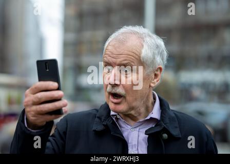Homme senior en état de choc devant son téléphone portable. Banque D'Images