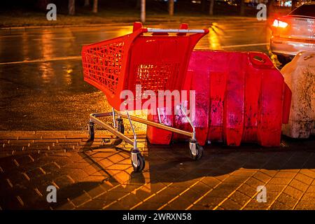 chariot d'épicerie rouge en plastique laissé un soir pluvieux près de la route Banque D'Images