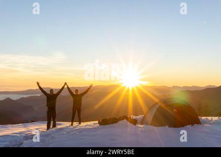 Couple célébrant à côté de tente dans la neige au coucher du soleil. Photo de haute qualité Banque D'Images