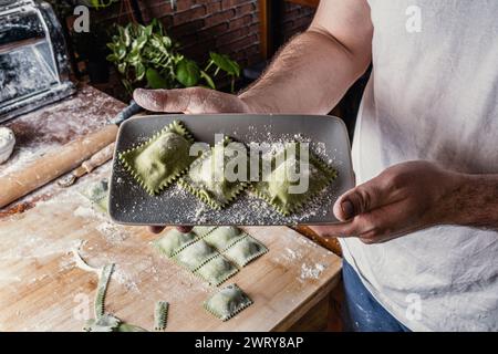 Gros plan des mains du chef tenant une assiette contenant des raviolis juste terminée et prête à être cuite. En arrière-plan, la table de travail était dégagée Banque D'Images