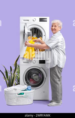 Heureuse femme senior mettant le linge dans la machine à laver sur fond violet Banque D'Images