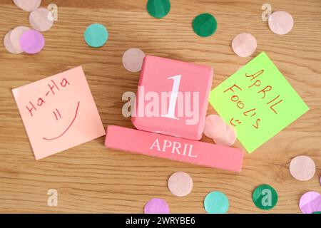 Calendrier cube avec la date du 1er AVRIL, autocollants en papier drôles et confettis sur fond en bois. Fête du Fool's Day d'avril Banque D'Images