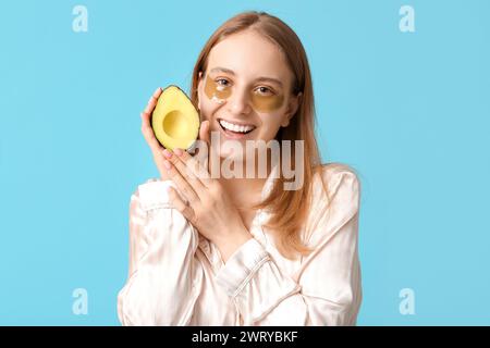 Jolie jeune femme en pyjama, avec des patchs sous les yeux et avocat sur fond bleu. Concept de cosmétologie Banque D'Images