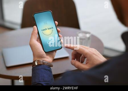 Homme utilisant un smartphone avec mot Cashback et icône de panier à l'intérieur, gros plan Banque D'Images