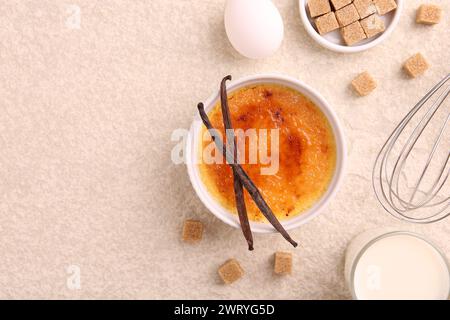 Délicieuse crème brûlée dans le bol et les ingrédients sur la table texturée légère, plat. Espace pour le texte Banque D'Images