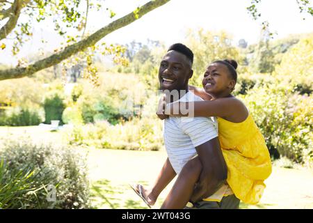 Un jeune père afro-américain offre à sa fille une balade en piggyback dans un parc ensoleillé Banque D'Images