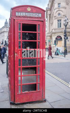 Boîte téléphonique rouge britannique traditionnelle, plus utilisée, sur le trottoir de la ville avec verre brisé et manquant et peinture écaillée et usée. Door AJAR. Banque D'Images