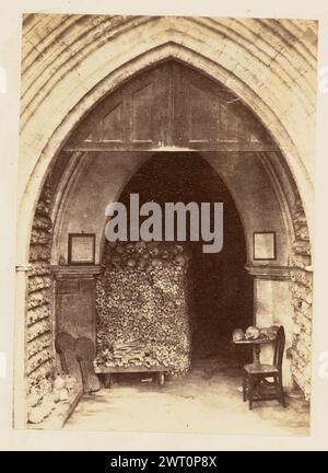 Entrée à une crypte. Inconnu, photographe vers 1864 vue d'une entrée d'une crypte en forme d'arche gothique, peut-être partie d'une église. Les murs intérieurs de l'arche sont bordés de rangées empilées de crânes humains, tandis que l'entrée elle-même est partiellement bloquée par plus d'os et de crânes. Également visible sur la zone inférieure droite de l'image est une petite table avec des crânes dessus et une chaise à côté de la table. Banque D'Images