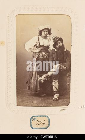Costumes italiens. Inconnu, photographe vers 1860–1880 portrait d'un homme et d'une femme vêtus de vêtements italiens traditionnels. La femme porte une robe à manches larges et un tablier brodé. Elle a un chapeau en tissu sur la tête qui pend dans le dos. L'homme est assis avec une jambe croisée sur l'autre. Il porte un chapeau rayé et a une barbe épaisse. (Recto, monture) centre inférieur, encre noire : 'costumes italiens' ; centre inférieur, encre noire : 'costumes italiens' ; (recto, page d'album) centre inférieur, image ci-dessous, encre noire sur étiquette bleue : 'no [in Blue text] 134'; Banque D'Images