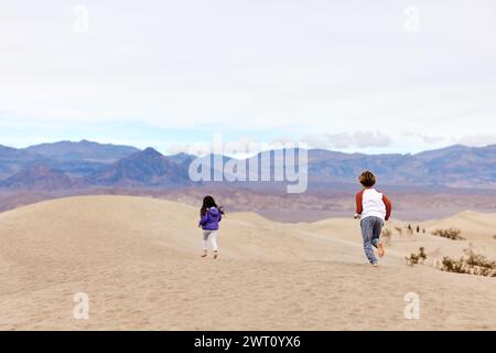 Vue arrière de frères et sœurs insouciants qui courent sur les dunes de sable de la vallée de la mort Banque D'Images
