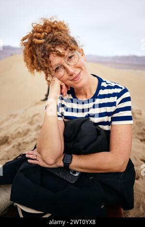 Portrait d'une femme rousse souriante assise sur une dune de sable à Death Valley Banque D'Images