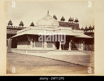 Tombe de Salim Chishti au Jama Masjid, Fatehpur Sikri. Attribué à Thomas A. Rust, photographe (anglais, 1841 - 1904) années 1870 vue du tombeau du cheikh Salim Chishti au Jama Masjid à Fatehpur Sikri. Le tombeau présente des fenêtres en treillis, des mosaïques géométriques, des crochets en serpentin et un grand dôme. Deux hommes sont assis de chaque côté de la porte, l'un protégeant ses yeux du soleil, et un troisième est partiellement visible allongé sur le dos derrière l'un des piliers soutenant le toit du portique. Banque D'Images