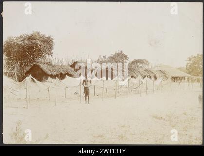 Filets de poisson suspendus à sec. Sir Henry 'Harry' Hamilton Johnston, photographe (anglais, 1858 - 1927) années 1890 Un homme debout devant des rangées de filets tendus sur des poteaux de bois, avec des maisons en chaume derrière eux. (Verso) centre supérieur, à l'encre : 'filets de poisson suspendus pour sécher./ ils n'aiment pas les poser sur le sable chaud/ comme il les brûle./ la ficelle est faite de diverses fibres/ arbustes et les mailles formées comme les nôtres./ (52)' ; centre, au crayon dans une main différente: 'Copyright/ Harry Johnson' [sic]' ; bords gauche et inférieur, au crayon, lignes de recadrage ; en bas à gauche, au crayon : '2699'; Banque D'Images
