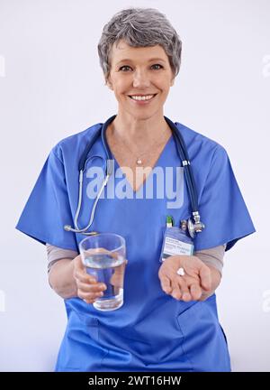 Femme senior, médecin et eau avec des pilules, soins de santé avec traitement médicamenteux et suppléments sur fond blanc. Vitamines, médicaments et Banque D'Images