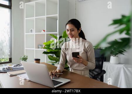 femme d'affaires utilisant un smartphone tout en travaillant sur ordinateur portable, synchroniser les données entre l'ordinateur et le gadget à la maison, utiliser les appareils d'entreprise et les affaires Banque D'Images