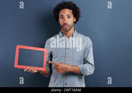 Tableau noir, portrait et homme avec la main pointant vers la maquette en studio pour l'annonce de nouvelles sur fond gris. Cadre, présentation ou visage de mâle Banque D'Images