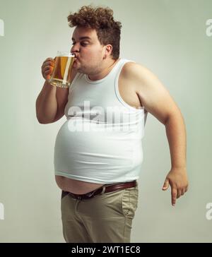 Chubby, gain de poids et bière pour homme en studio avec de l'alcool pour les habitudes malsaines, plus la taille et l'humour. Personne en surpoids avec verre à la main et Banque D'Images