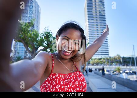 Un jeune homme africain heureux qui prend un selfie en regardant la caméra et en la faisant signe, en partageant les médias sociaux. Banque D'Images