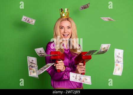 Photo d'excité superbe dame couronne dorée tirer des billets de dollar pistolet d'argent isolé sur fond de couleur verte Banque D'Images