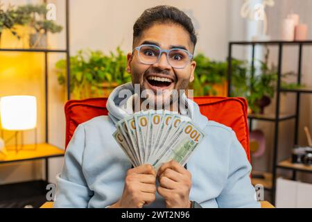 Homme d'affaires heureux heureux et riche réussi Indien comptant l'argent encourageant avec des profits élevés, célébrer la victoire de jeu de loterie, satisfait des revenus de richesse salaire, tenant des dollars en espèces dans les mains à la maison Banque D'Images