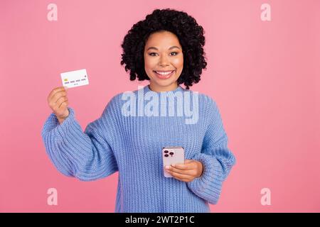 Portrait photo de jolie jeune fille tenir la carte de crédit de l'appareil habillé élégant indice tenue tricotée isolée sur fond de couleur rose Banque D'Images