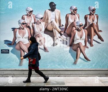 Londres, Royaume-Uni. 15 mars 2024. Une femme passe une affiche devant un magasin de vêtements de créateurs pour hommes près de Saville Row. Sean Dixon, directeur général du tailleur sur mesure de Savile Row Richard James, a déclaré que les magasins britanniques sont actuellement perdants face aux maisons de couture dans des endroits tels que Paris et Milan et est parmi plusieurs dans la communauté des affaires appelant à la suppression de la soi-disant taxe de séjour. Il y a trois ans, le gouvernement a supprimé les achats sans TVA pour les touristes, une mesure qui a particulièrement touché les détaillants de luxe qui comptent sur les touristes aisés. Credit : Stephen Chung / Alamy Live News Banque D'Images