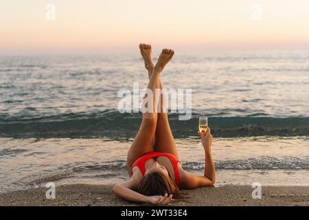 Femme en maillot de bain rouge profitant d'une boisson au coucher du soleil au bord de la mer Banque D'Images