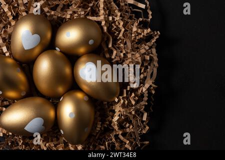Oeufs dorés dans le nid de papier sur la table sombre. Banque D'Images