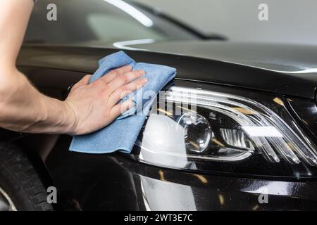 Jeune homme à la main nettoyant la lampe frontale de la voiture moderne dans le studio d'esthétique, détailler le concept de voiture Banque D'Images