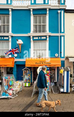 Un homme et son chien passent devant une boutique de cadeaux avec un grand logo Ice Cream au-dessus de l'entrée. Vue Portrait Banque D'Images