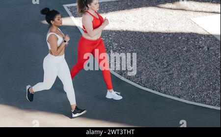 Prise de vue d'en haut de deux femelles courant ensemble à l'extérieur. Angle élevé de deux amies jogging ensemble portant des vêtements de sport de différentes couleurs. Banque D'Images