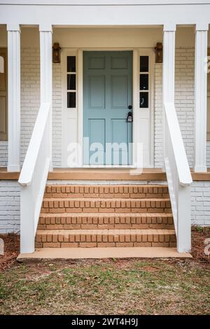 L'entrée extérieure avant d'une porte d'entrée nouvellement peinte bleu aqua sur une maison de style ranch en brique blanche avec des marches en briques. Banque D'Images