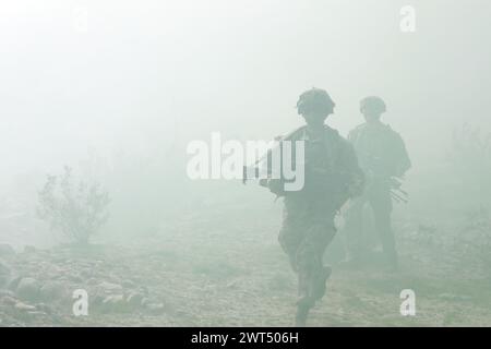 Parachutistes de l'armée américaine, affectés au 2nd Battalion, 508th Parachute Infantry Regiment, 2nd Brigade combat Team, 82nd Airborne Division, se déplacer à travers un terrain désertique vers un objectif au sein d'un village d'opérations militaires sur un terrain urbain tirant parti d'un transport d'équipement polyvalent de petite armée américaine pendant l'expérimentation d'intégration humaine-machine dans le cadre du projet convergence - Capstone 4, Fort Irwin, Calif., 13 mars 2024. Le SMET est un huit roues, permettant la technologie robotique servant de «mule robotique» avec une large gamme de flexibilité pour fonctionner dans le combat, le soutien au combat et le service de combat Banque D'Images