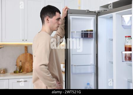 Homme bouleversé près d'un réfrigérateur vide dans la cuisine Banque D'Images