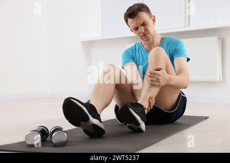 Homme souffrant de douleurs aux jambes sur tapis à l'intérieur Banque D'Images