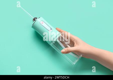 Main féminine tenant l'irrigateur oral sur fond turquoise Banque D'Images