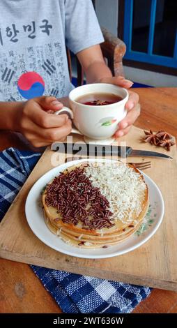 Une photo de quelqu'un mangeant un mini martabak et buvant une tasse de thé sur une table en bois Banque D'Images