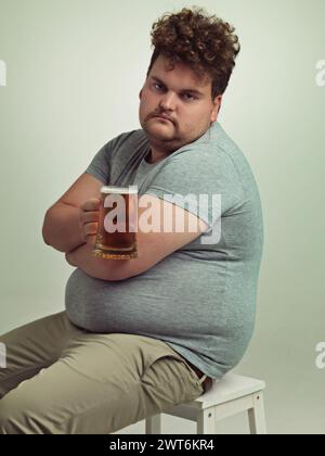 Portrait, bras croisés et homme de taille plus avec de l'alcool pour habitude malsaine, prise de poids grave en studio de fond blanc. Visage, bière et mâle Banque D'Images