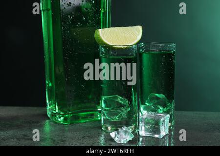 Absinthe dans des verres à dose avec de la citron vert et des glaçons sur une table texturée grise, gros plan. Boisson alcoolisée Banque D'Images