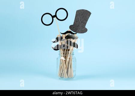 Faux moustaches en papier, lunettes, chapeau et pailles dans le pot sur fond bleu clair Banque D'Images