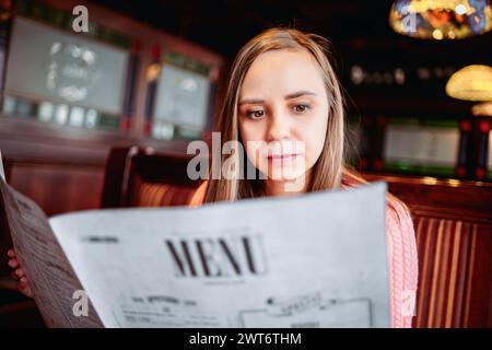 Une femme est assise à une table, lisant attentivement un menu Banque D'Images