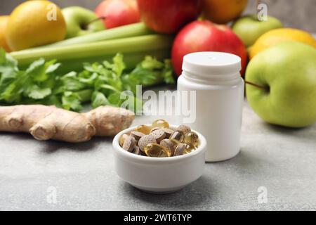 Compléments alimentaires. Bouteille blanche vierge et différentes pilules dans un bol près des produits alimentaires sur une table texturée grise, gros plan Banque D'Images