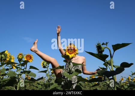 jeune fille jouant dans un champ de tournesols cachant son visage derrière une fleur, espace de copie Banque D'Images