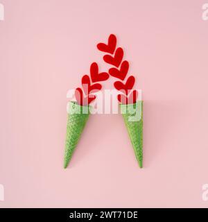 Crème d'amour d'été. Mise en page créative faite avec des coeurs rouges et des cônes de crème glacée gaufrés verts sur fond rose. Concept minimal d'amour estival. Banque D'Images